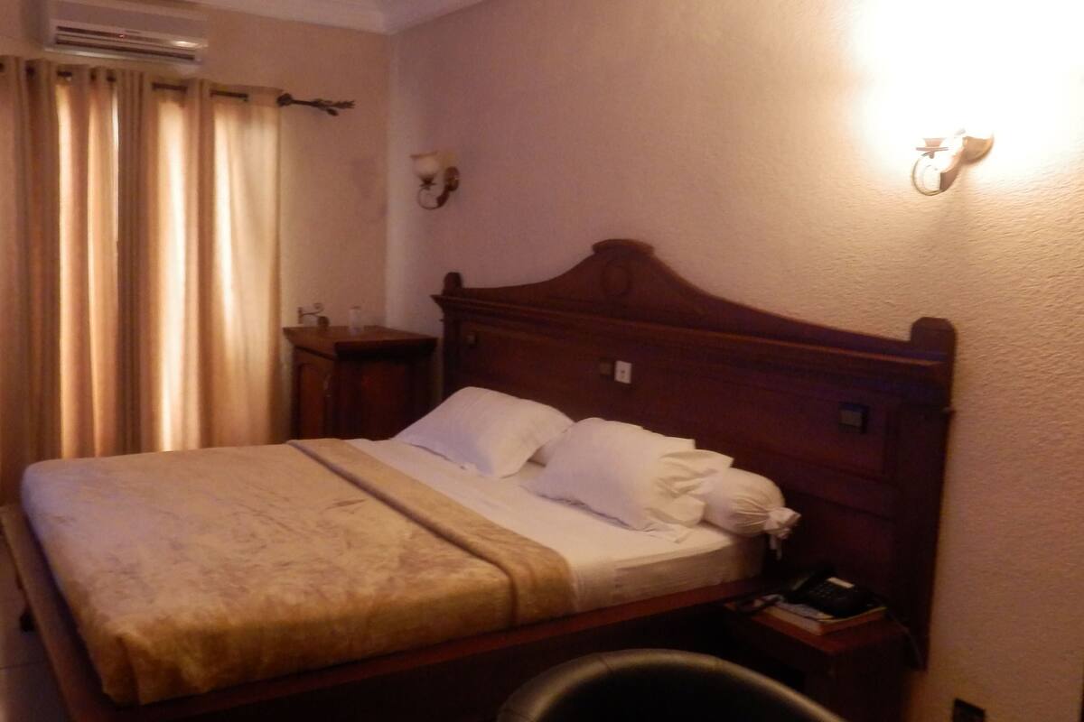 A neatly made bed with a wooden headboard, a bedside table with a lamp, and a wall-mounted light fixture.
