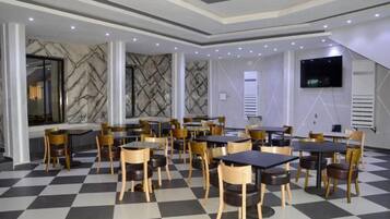 Un restaurante con piso a cuadros, varias mesas y sillas, detalles de pared de mármol y un televisor de pantalla plana montado en la pared.