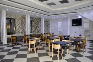 A restaurant with checkered flooring, multiple tables and chairs, marble wall accents, and a flat-screen TV mounted on the wall. - Vallée des Princes Hôtel (Douala)