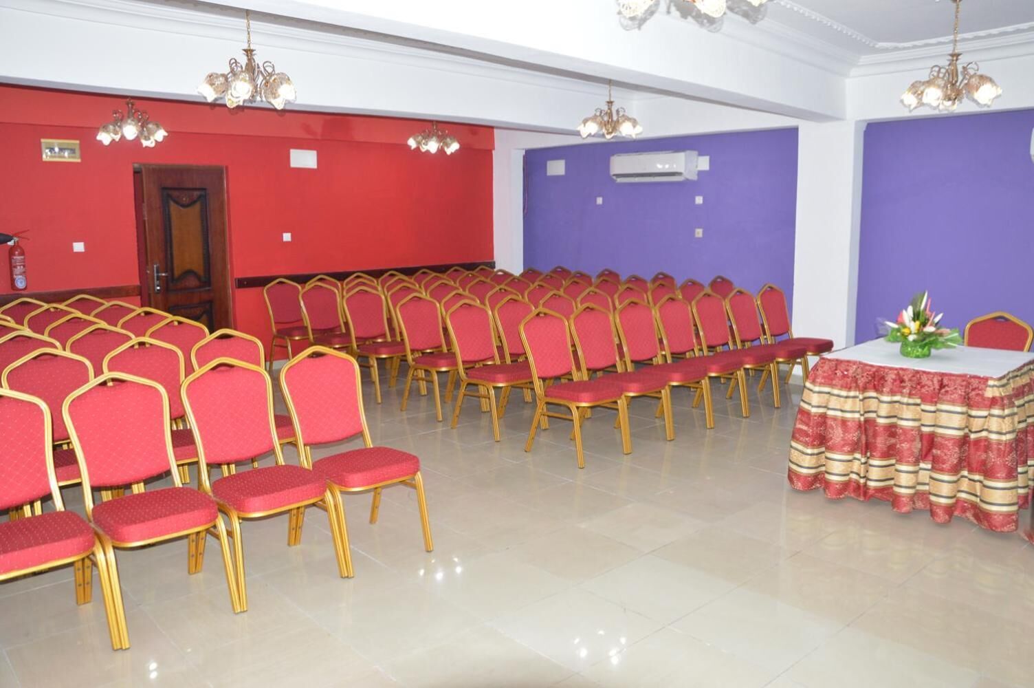 A conference room with rows of red chairs and a table with a patterned tablecloth.
