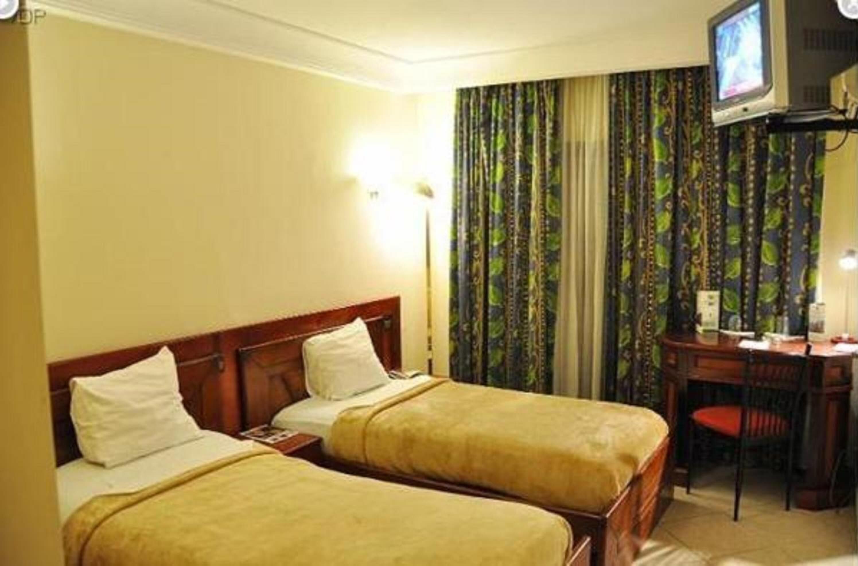 Habitación de hotel con dos camas, un escritorio con silla y un televisor en la pared.