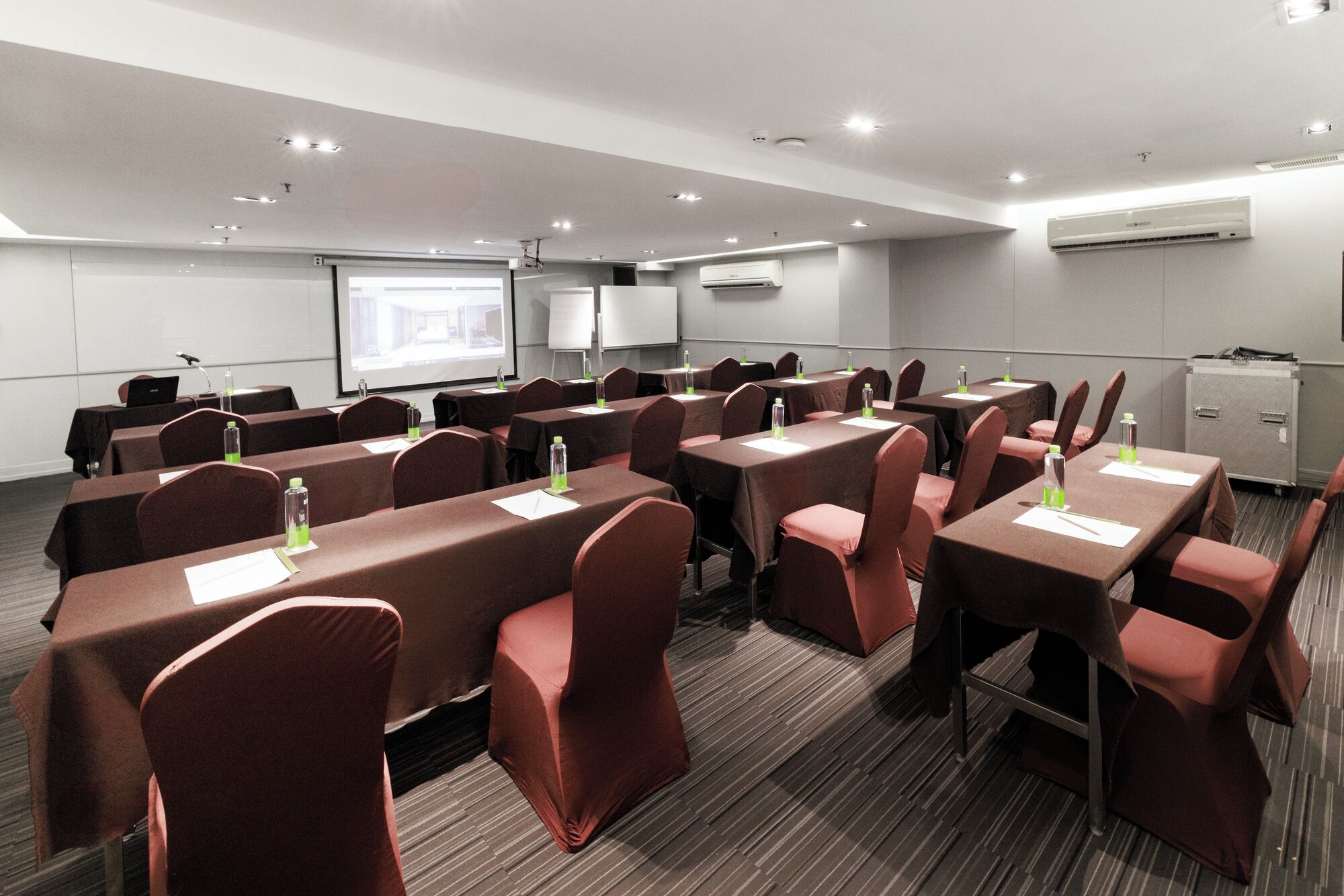 Una sala de conferencias con mesas, sillas, una pantalla de proyector y un equipo de aire acondicionado.