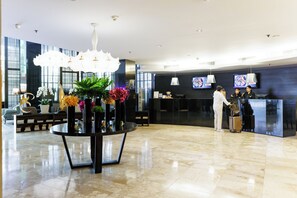 A hotel lobby with a reception desk, a large chandelier, and a reception area with a counter and monitors. - S15 Sukhumvit Hotel (Bangkok)