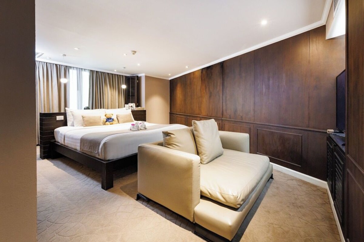 Habitación de hotel con una cama doble, un sofá, un televisor y paneles de madera en las paredes.