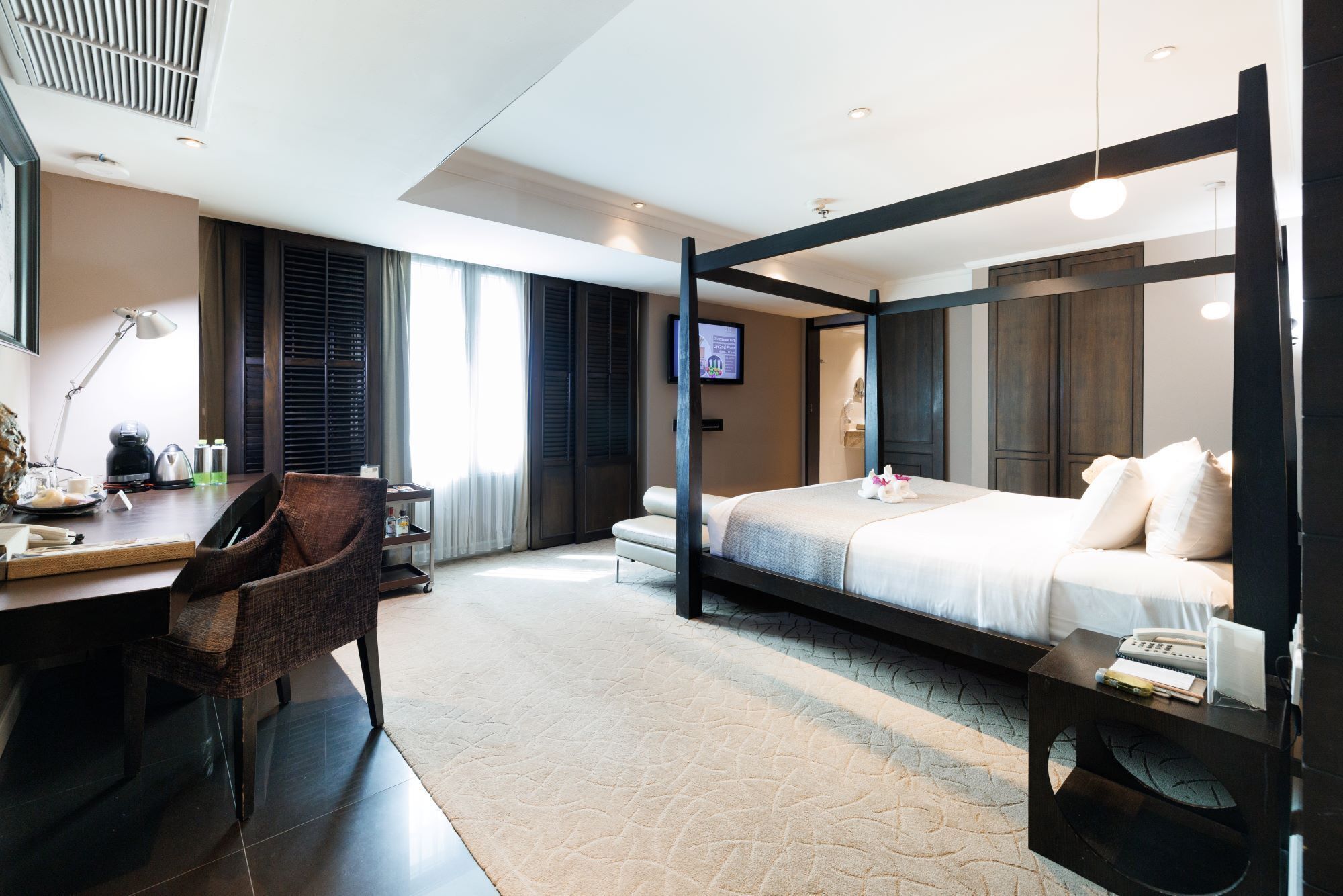Una habitación de hotel moderna con una cama con dosel, un escritorio con silla, un televisor de pantalla plana y una mesita de noche pequeña.