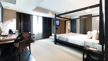 Una habitación de hotel moderna con una cama con dosel, un escritorio con silla, un televisor de pantalla plana y una mesita de noche pequeña.