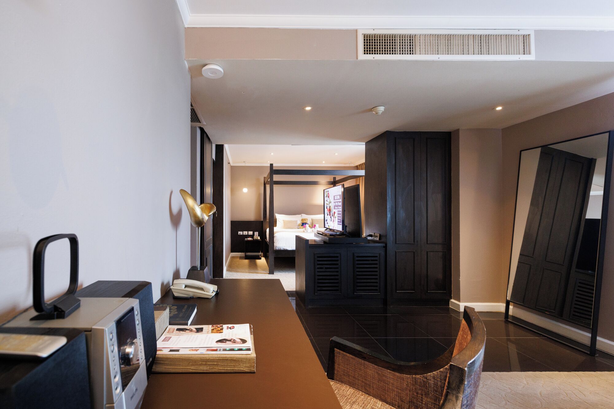 A hotel lobby with a reception desk, a seating area, a television, and a hallway leading to a bedroom.