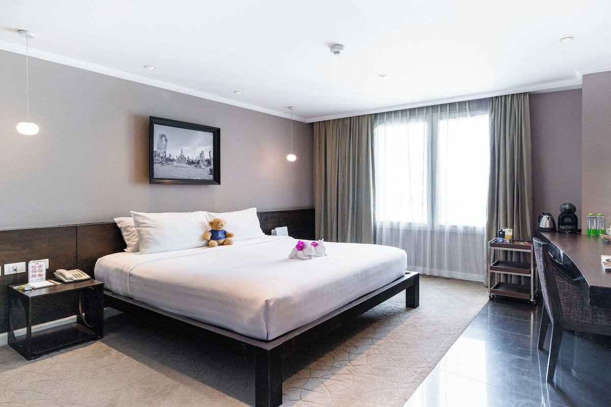 Une chambre d’hôtel avec un grand lit, des tables de chevet, un bureau avec une chaise, une télévision et une fenêtre avec des rideaux.