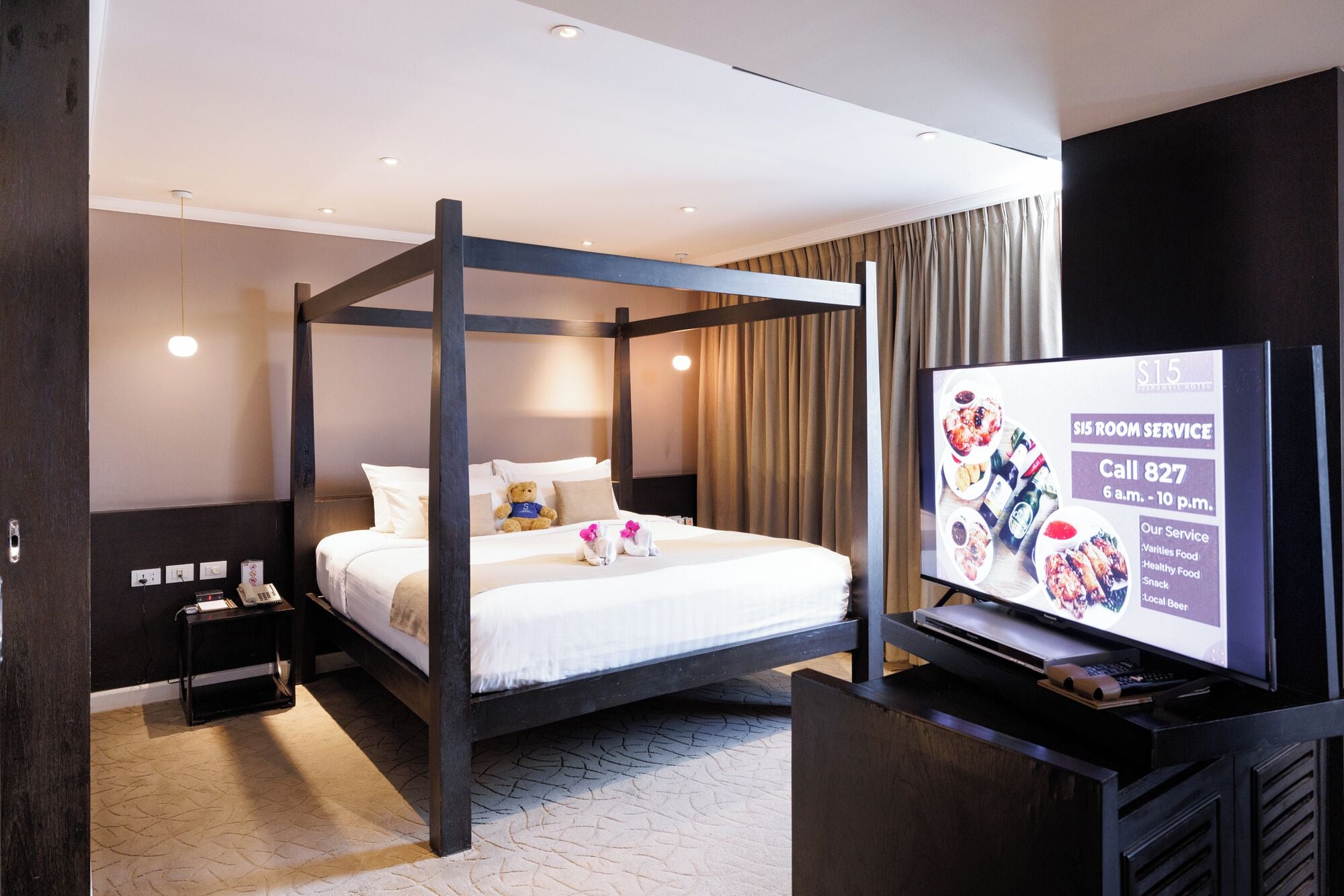 Een hotelkamer met een hemelbed, een televisie op een standaard, een nachtkastje en een stopcontact.