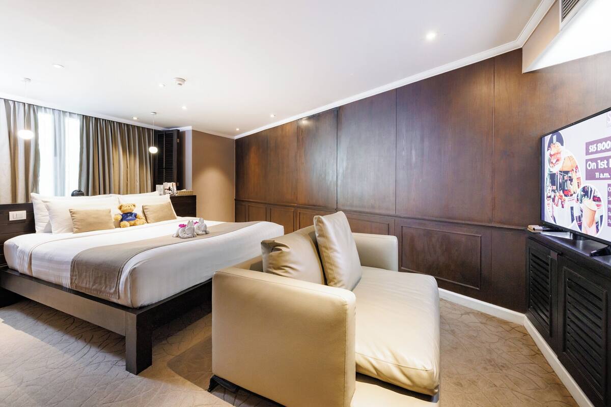 Une chambre d’hôtel avec deux lits, un canapé, une télévision et un écran fixé au mur.