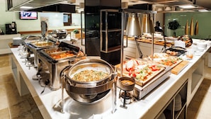 Montaje de bufé con diferentes estaciones de comida, que incluyen una barra de pasta, una barra de ensaladas y una zona de parrillada.