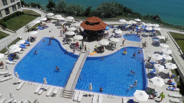 A large outdoor swimming pool with multiple lanes, surrounded by sun loungers and umbrellas, and a view of the sea. - Byala Beach Resort (Byala)
