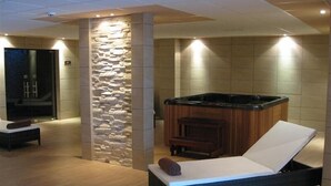 A spa room with a stone wall, a hot tub, and a reclining chair. - Byala Beach Resort (Byala)