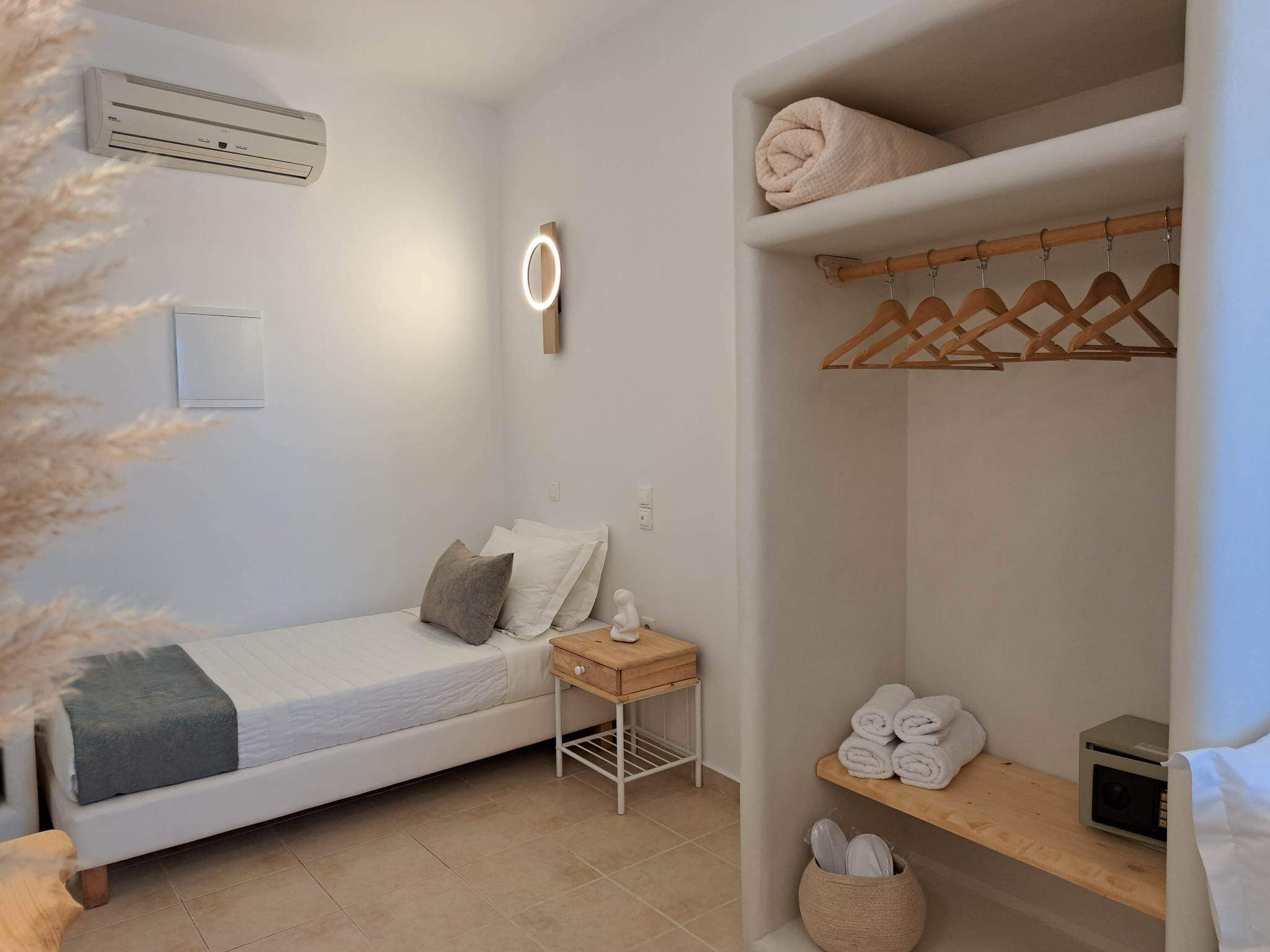 A bedroom with a bed, bedside table, and a wardrobe with hanging clothes.