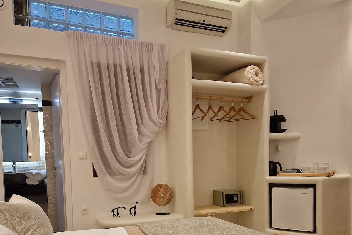 Una habitación de hotel moderna con cama, una kitchenette pequeña, un vestidor y un baño visible a través de una puerta abierta.