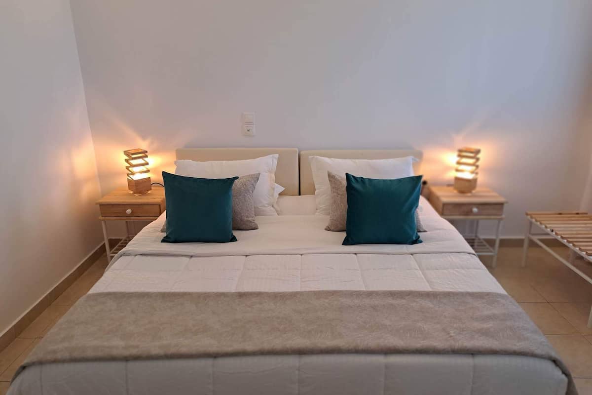 Una cama bien hecha con dos almohadas, una mesita de noche con una lámpara y un estante de madera.