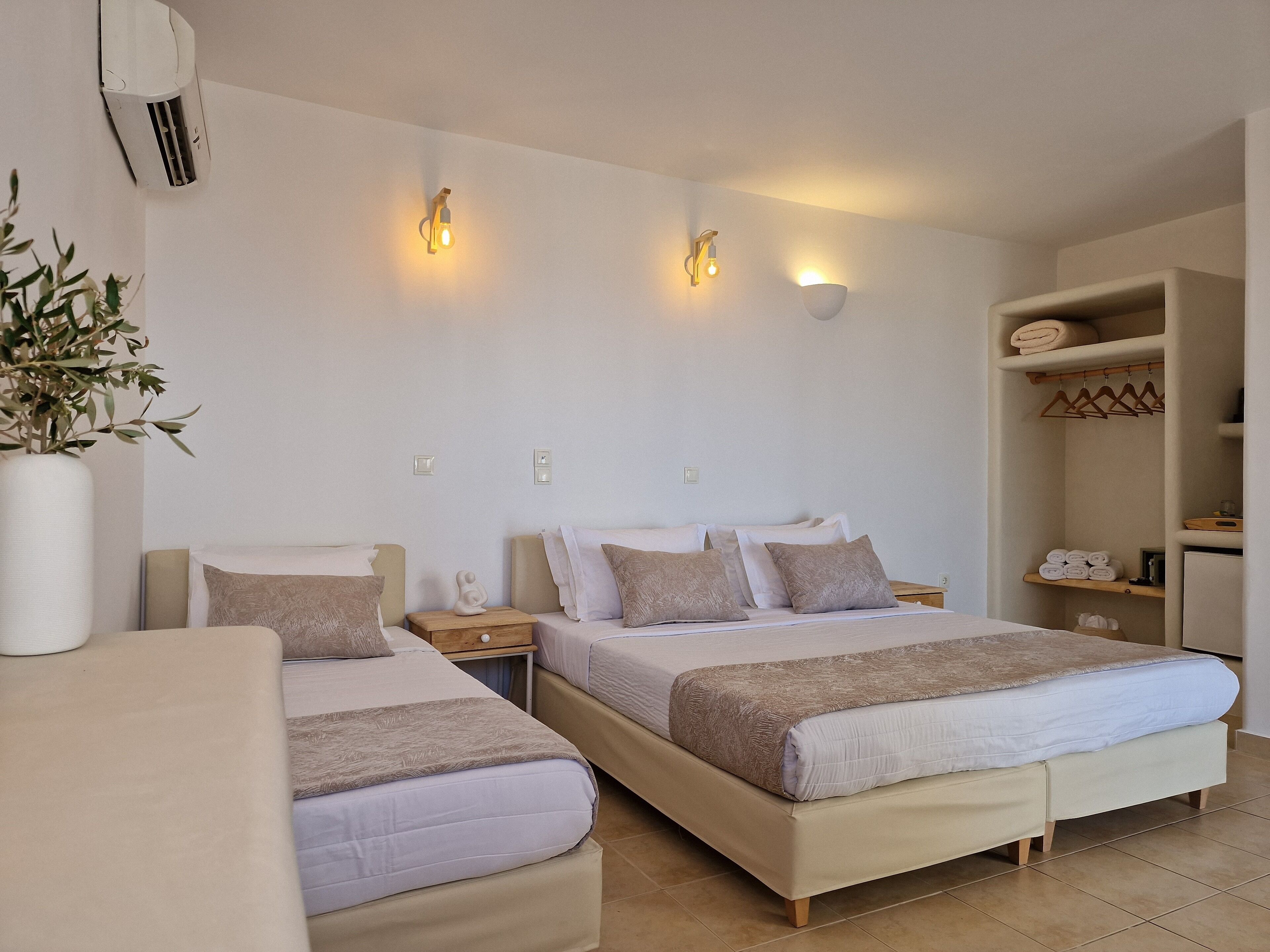 Habitación de hotel con dos camas, una mesita de noche, aire acondicionado instalado en la pared y un estante con toallas.