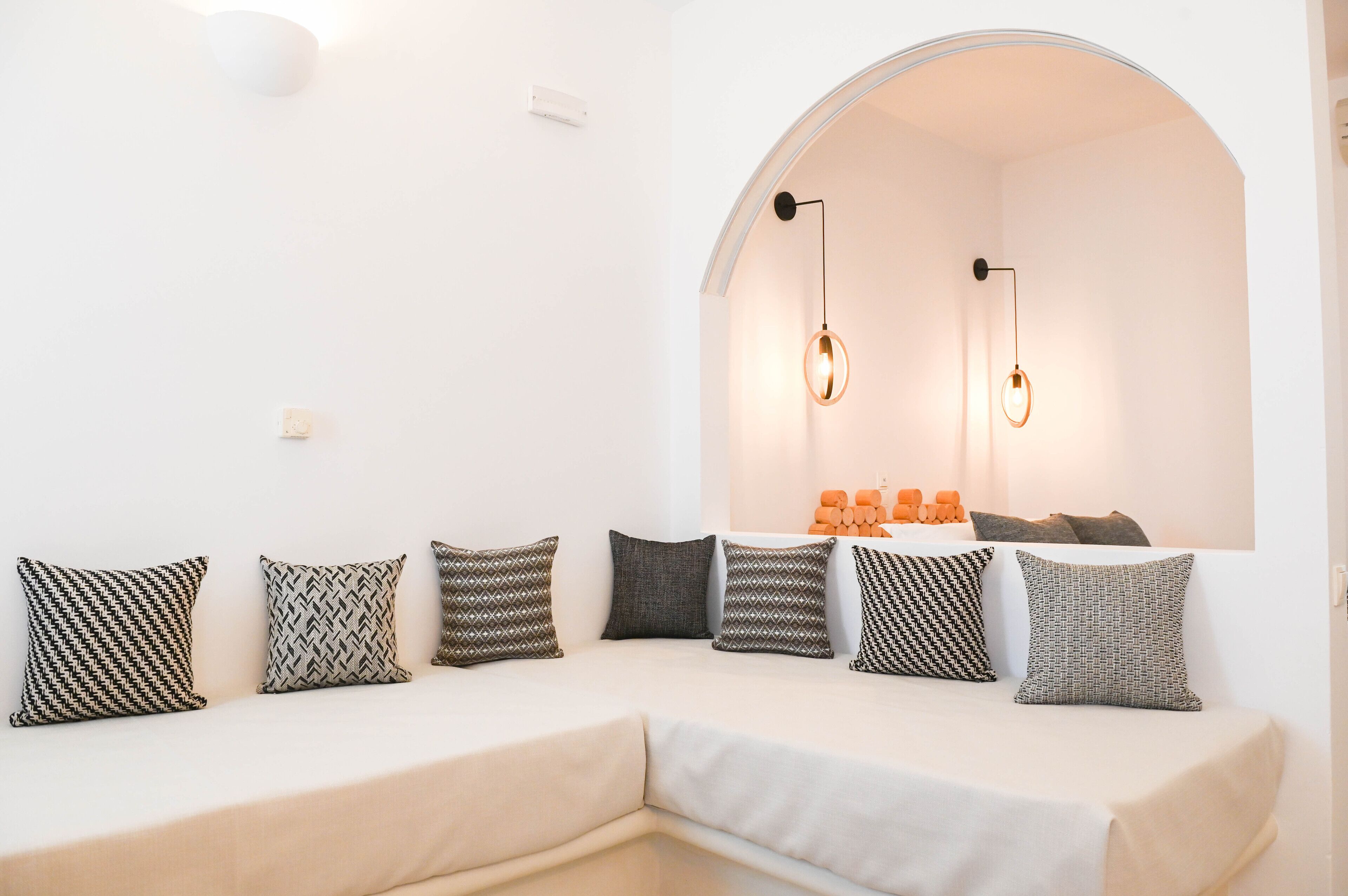 A modern, minimalist living room with a white sofa, patterned cushions, and a large arched window.