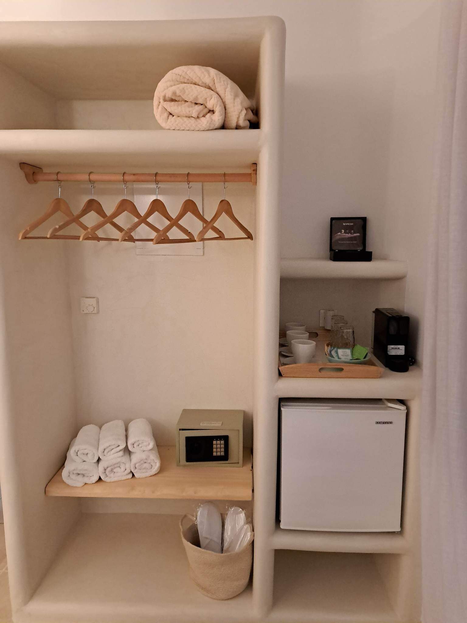 Una habitación compacta con armario, un refrigerador pequeño y repisas con artículos de aseo.