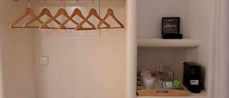 Una habitación compacta con armario, un refrigerador pequeño y repisas con artículos de aseo.
