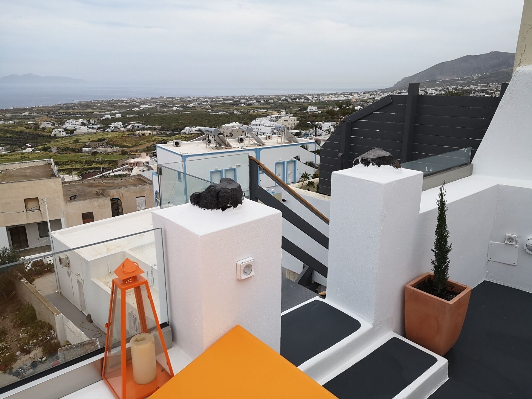Una terraza en la azotea con vistas a un pueblo costero, una pequeña planta en maceta y un farol.