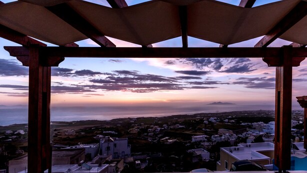 Vista de uma área coberta com vista para uma cidade costeira, prédios e um pôr do sol.