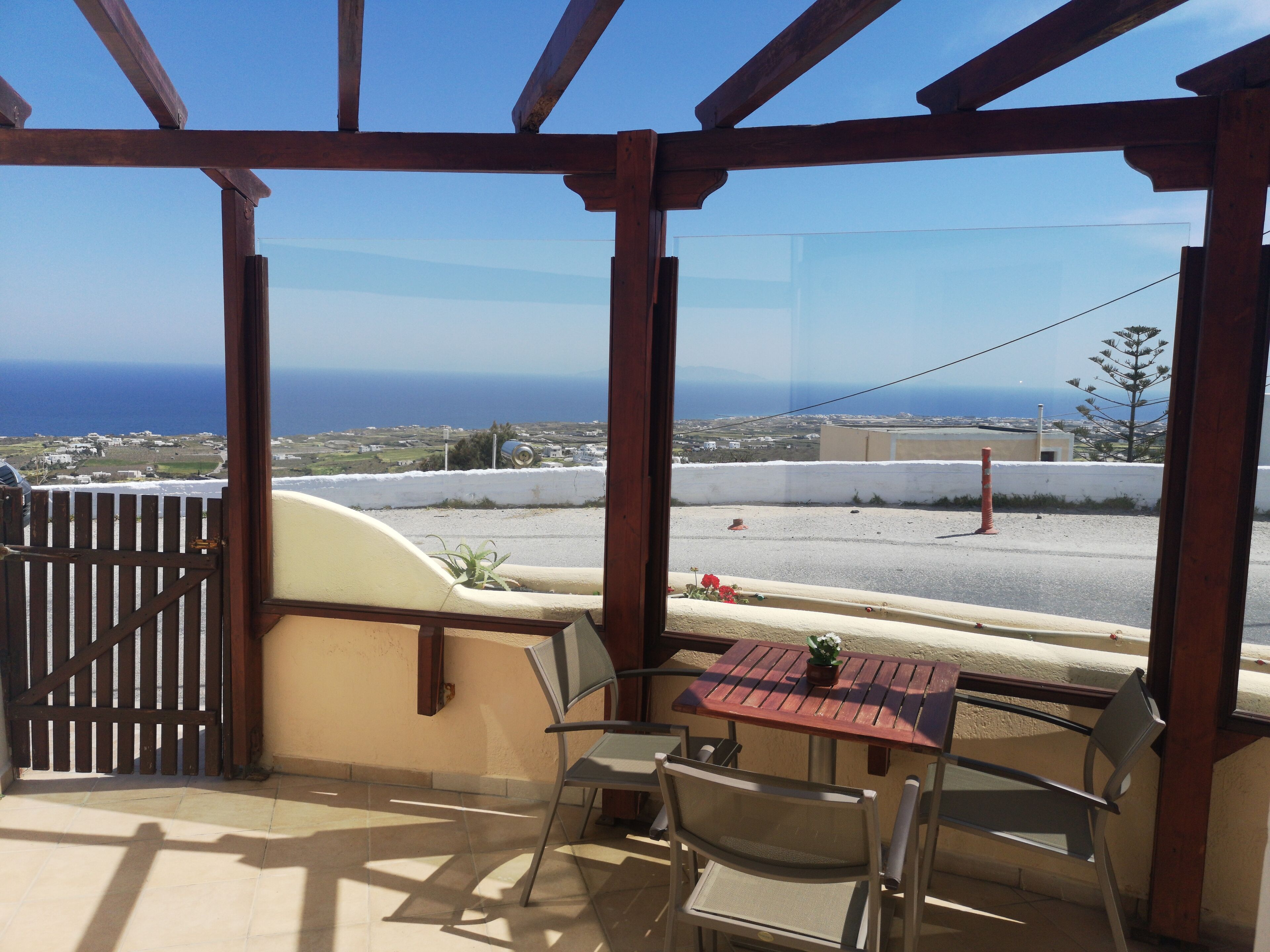 A balcony with a table and chairs, a view of the sea, and a wooden pergola structure.