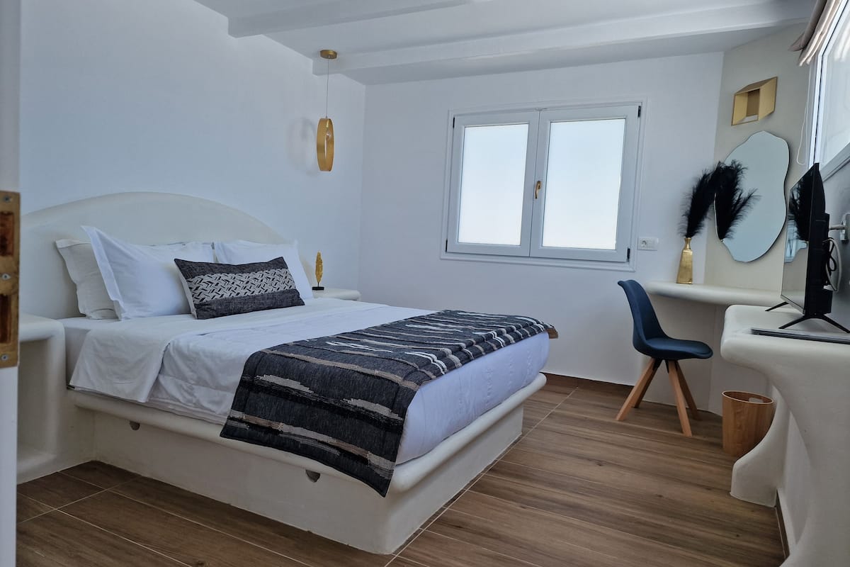 Un dormitorio con cama, mesita de noche, silla y escritorio con computadora.