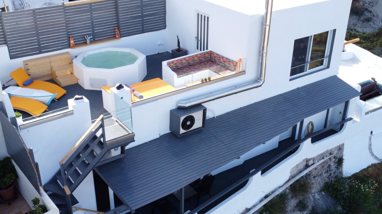 A modern rooftop with a hot tub, outdoor seating, and a staircase leading to an upper level.