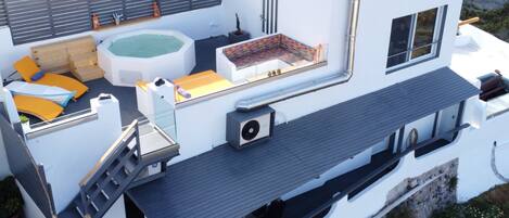 A modern rooftop with a hot tub, outdoor seating, and a staircase leading to an upper level.