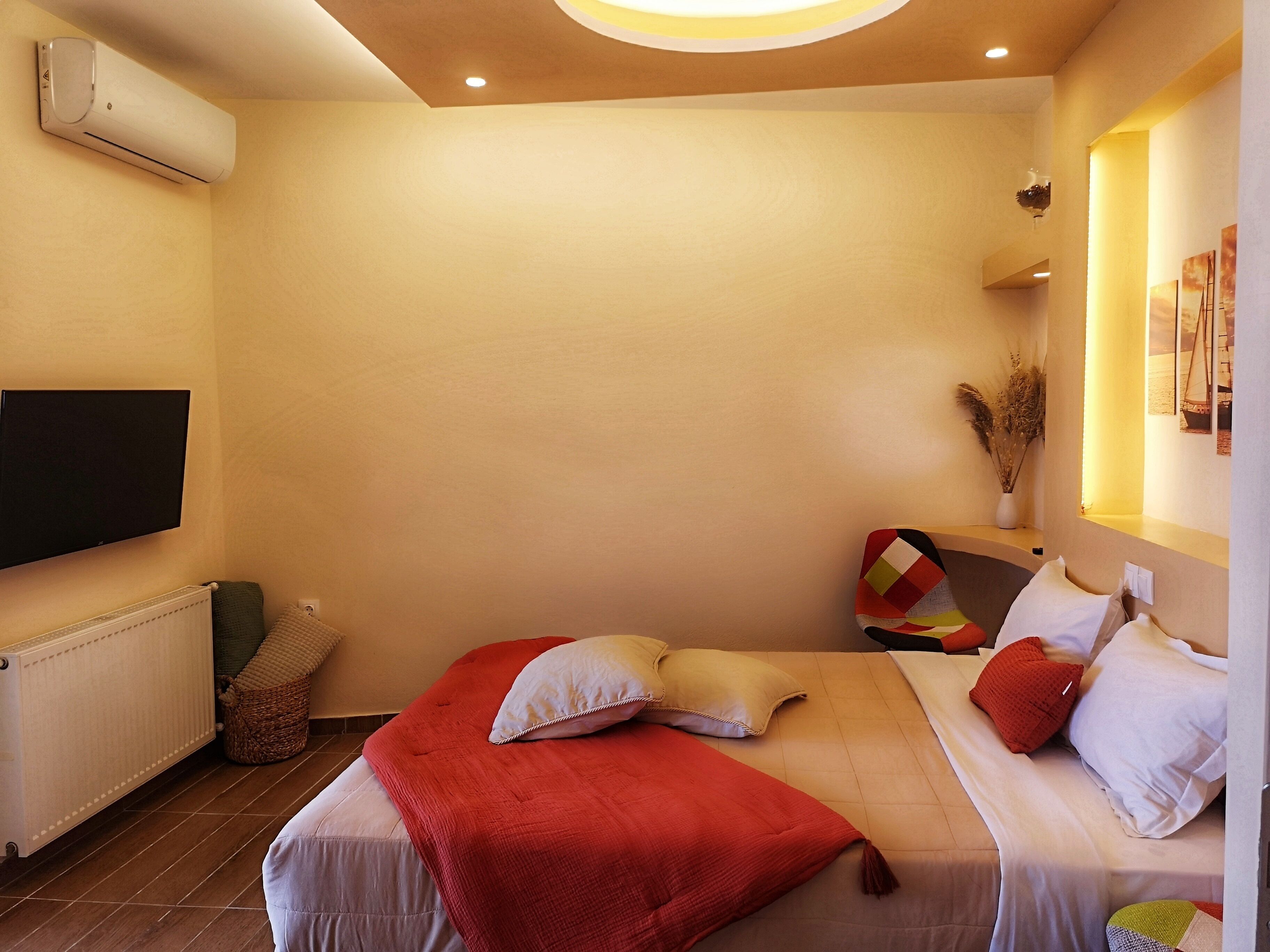 Une chambre à coucher comprenant un lit, des oreillers, un téléviseur à écran plat, un radiateur et un climatiseur fixé au mur.
