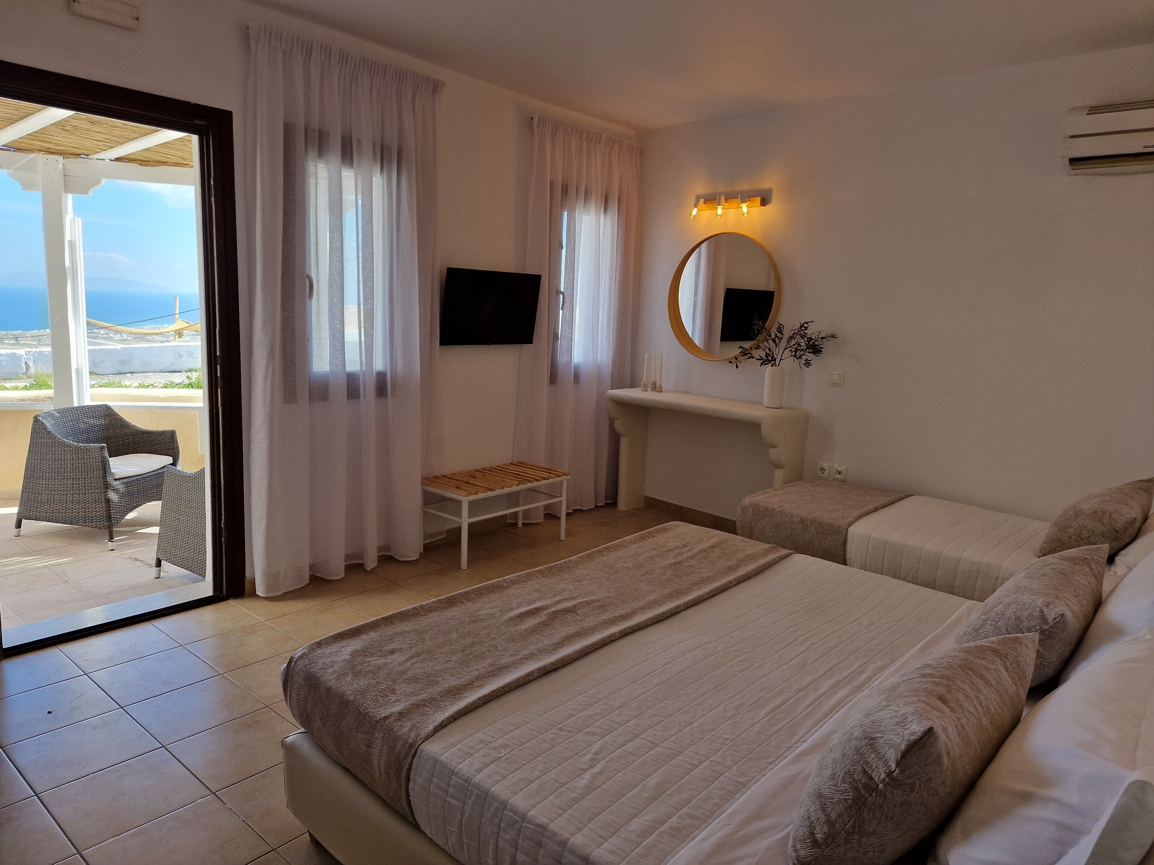 A hotel room with two beds, a TV, a small table, a chair, and a view of the sea.