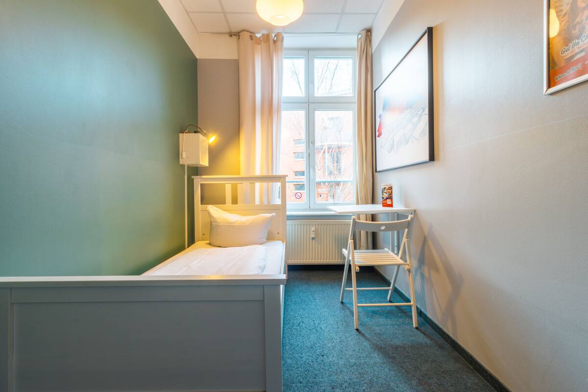 A small, neatly arranged room with a single bed, a desk, and a chair.