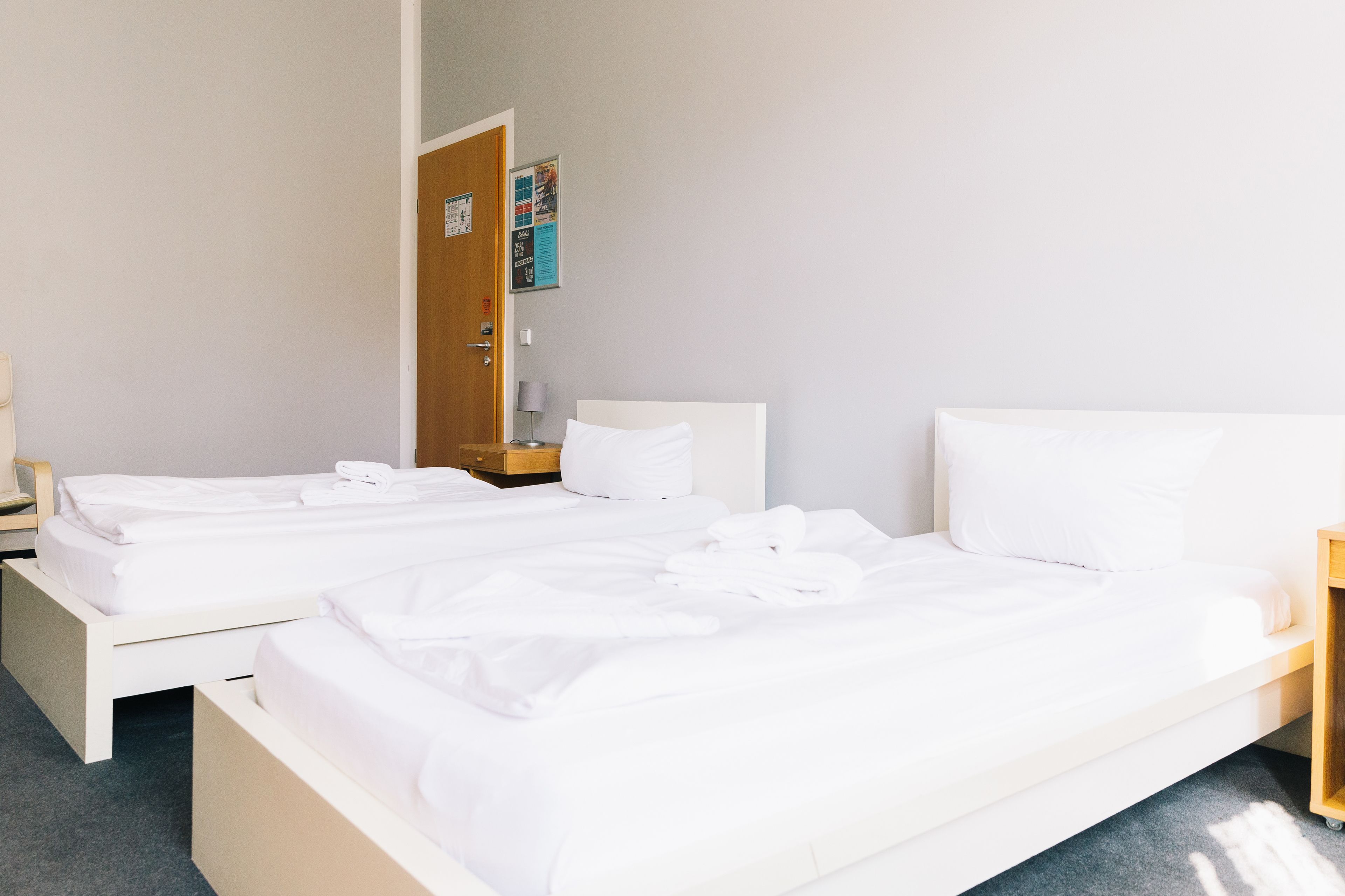 Ein Hotelzimmer mit zwei Betten, einem Holznachttisch, einer Lampe und einer Tür mit einem Poster.
