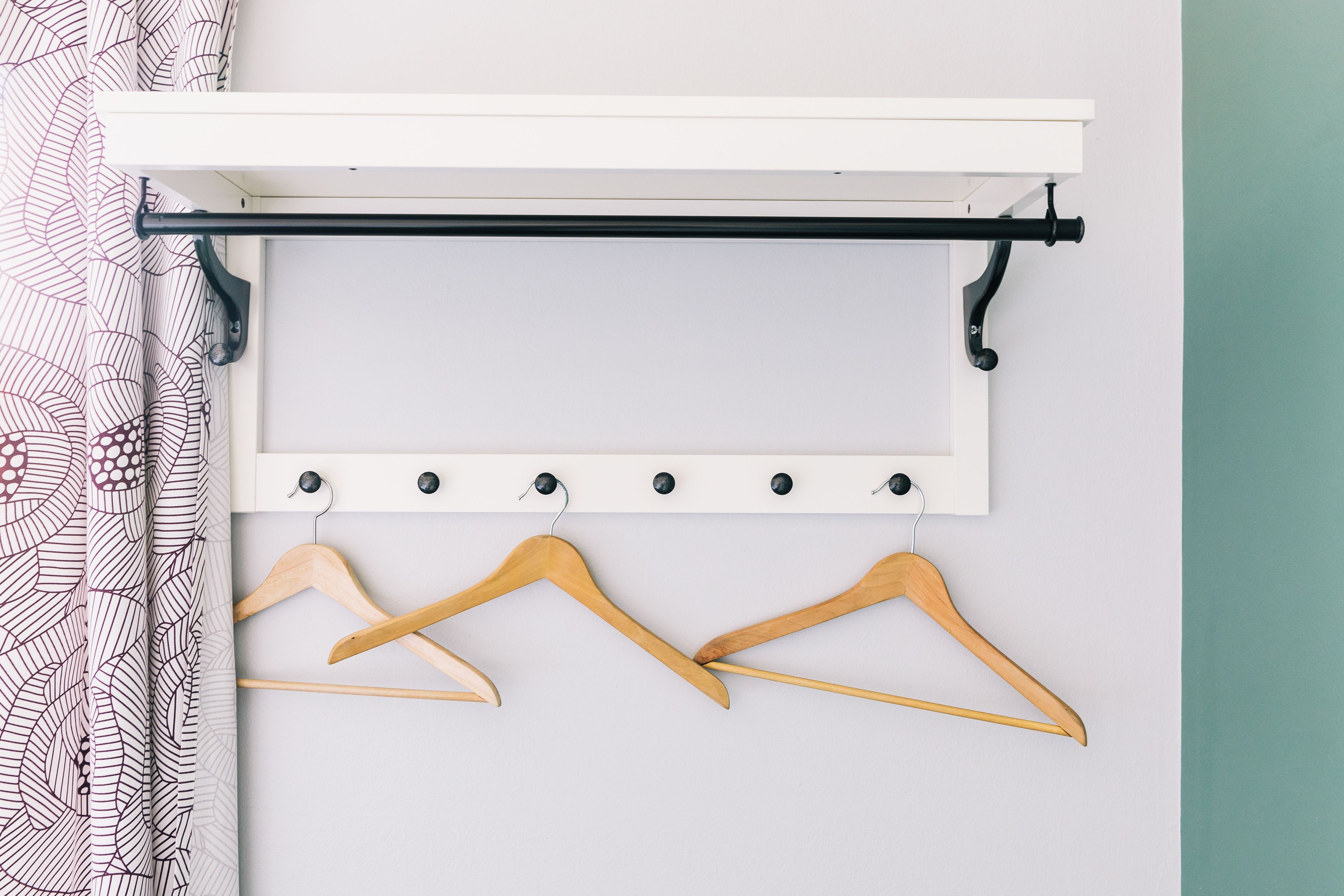 A white wall with a black metal rod and wooden hangers.