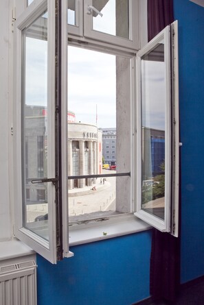 A room with a large window overlooking a cityscape, including a building with columns and a street with vehicles. - St Christopher's Berlin Alexanderplatz - Hostel (Berlin)