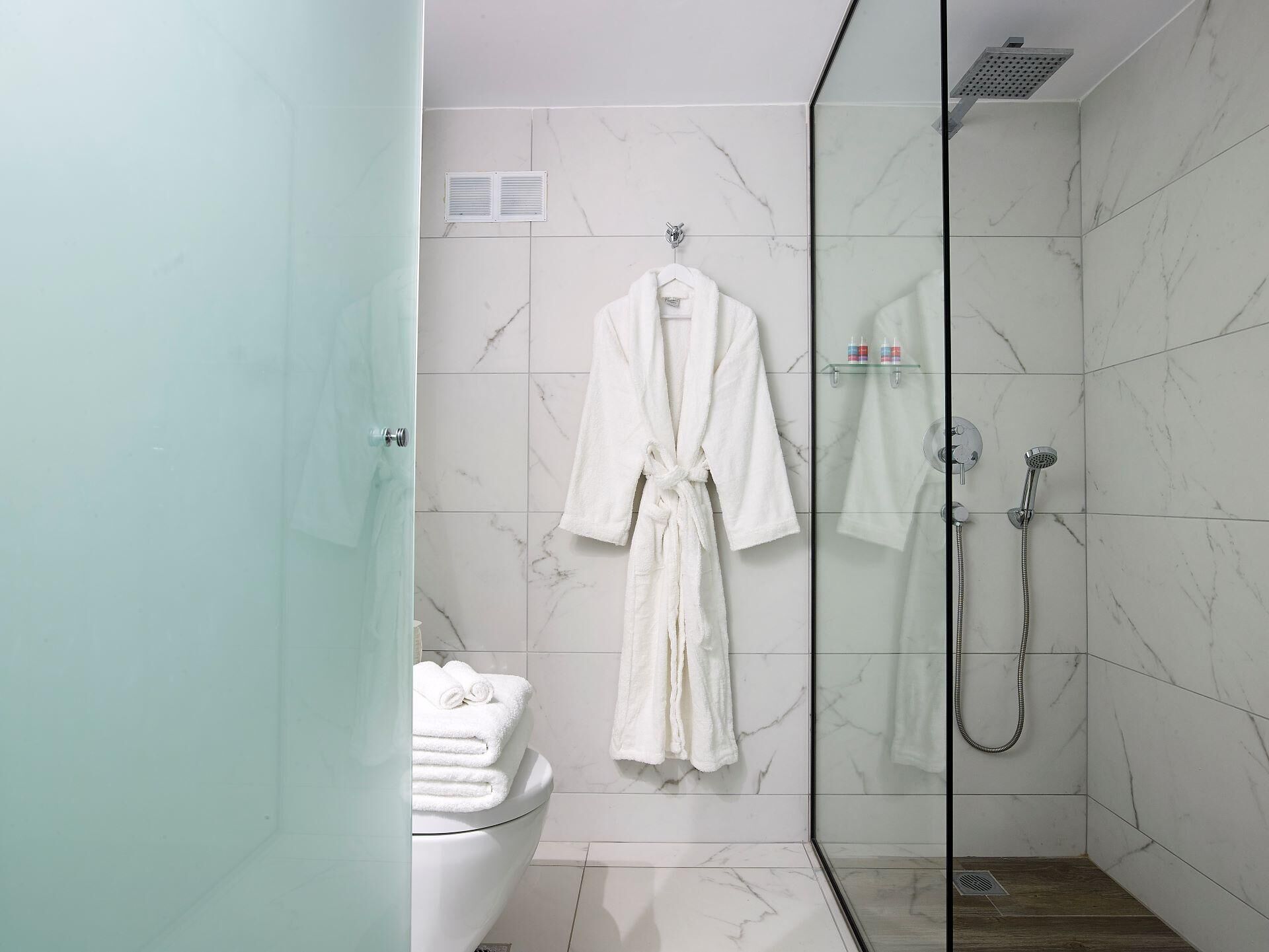A modern bathroom with a glass-enclosed shower, a white toilet, and a white bathrobe hanging on the wall.