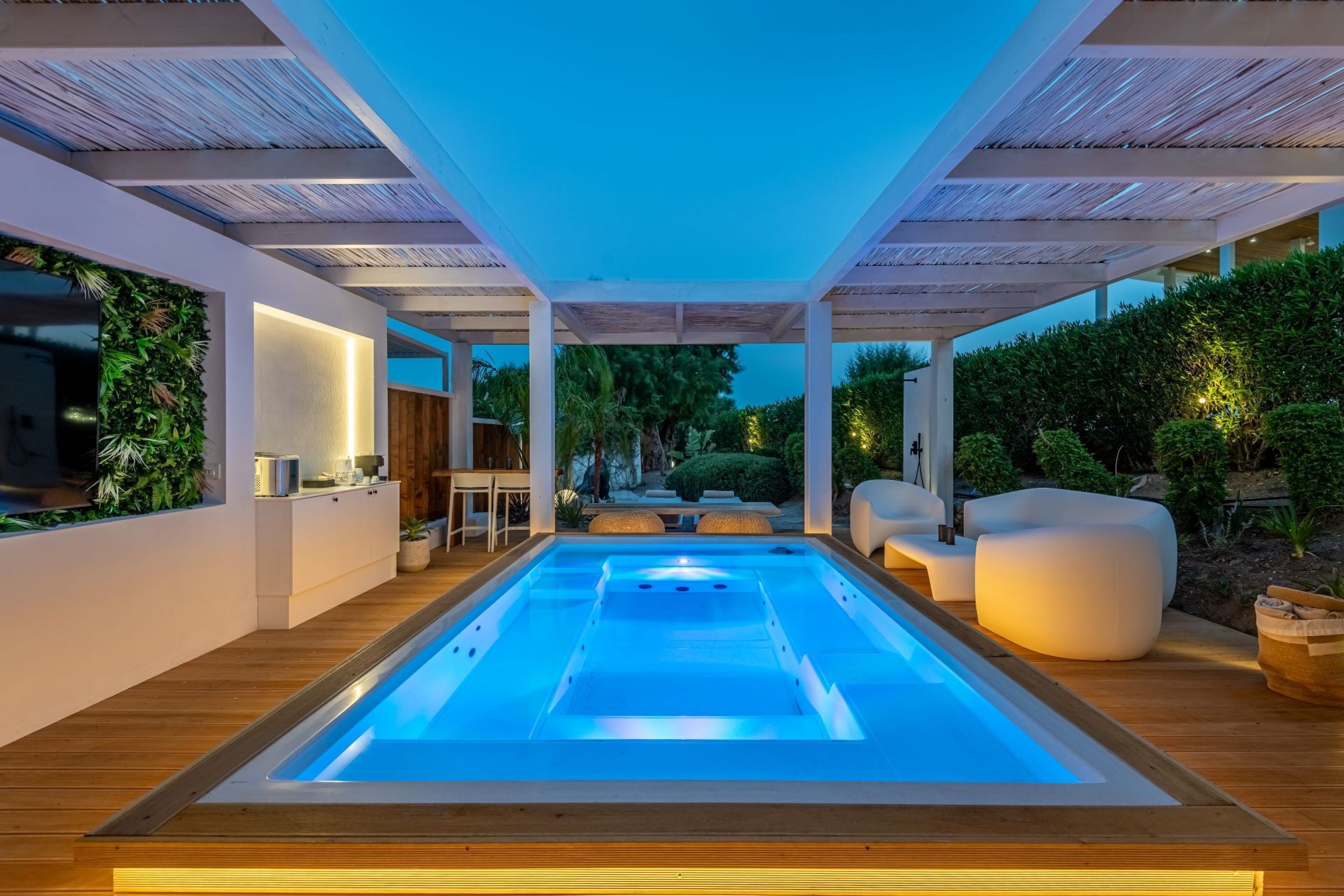 Un área de piscina interior moderna con cubierta de madera, asientos y vista al jardín.