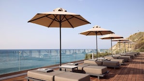 Een terras met loungebedden en parasols met uitzicht op een wateroppervlak en een brug.
