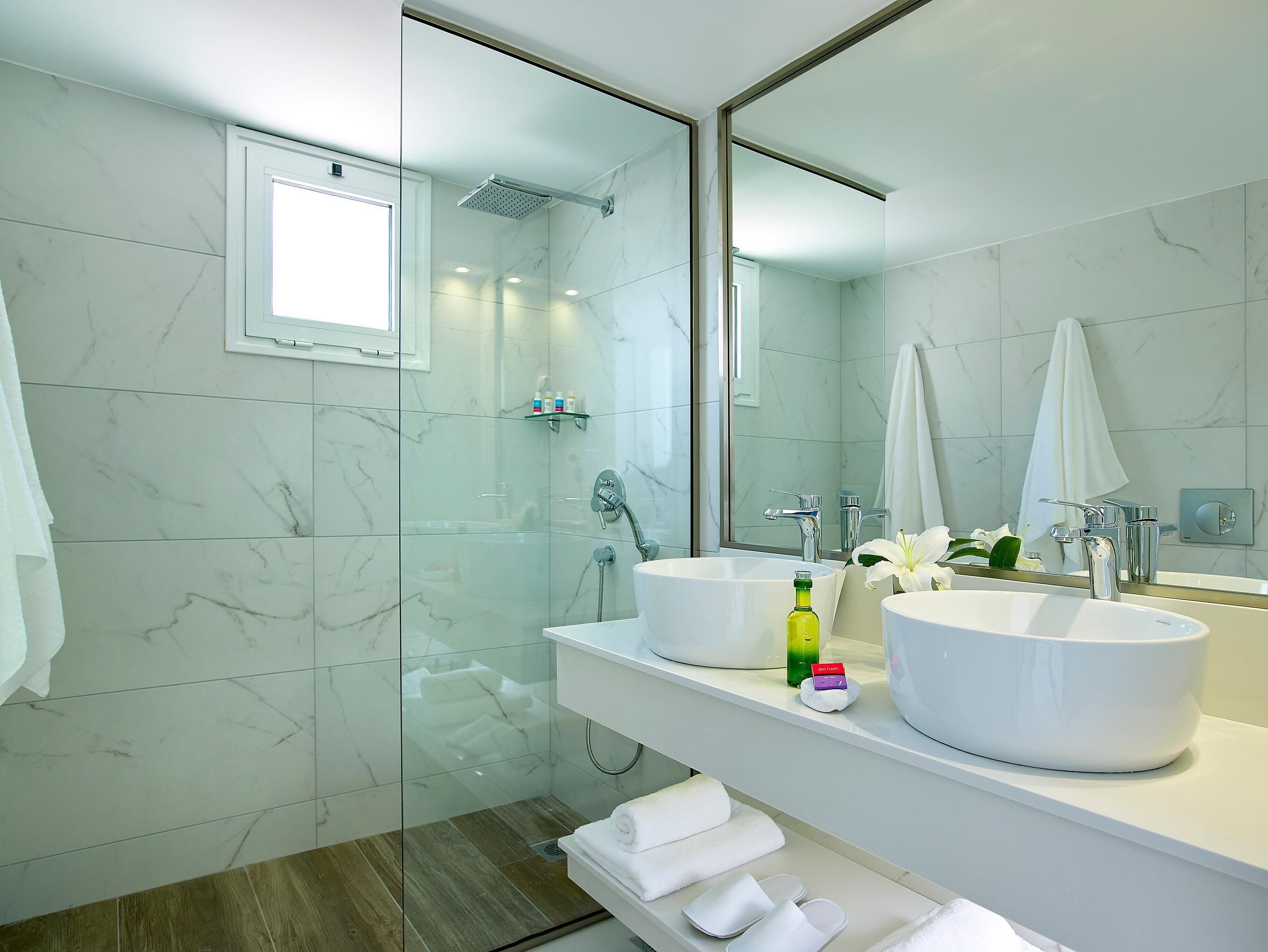 A modern bathroom with two sinks, a glass shower enclosure, and a large mirror.