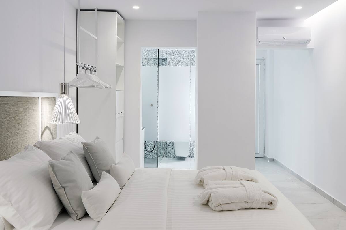 A modern hotel room with a large bed, a walk-in closet, and a bathroom visible through a glass door.
