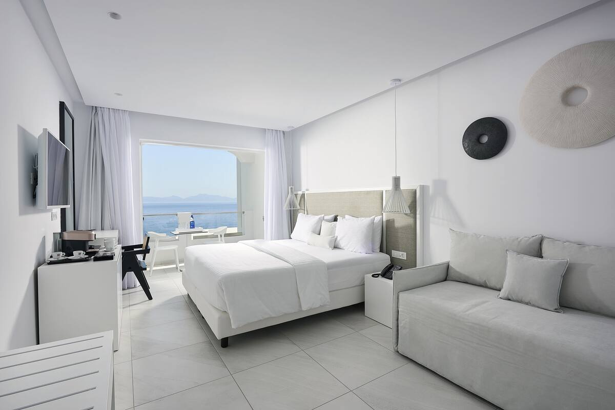 A modern hotel room with a large bed, a sofa, a desk, and a TV.