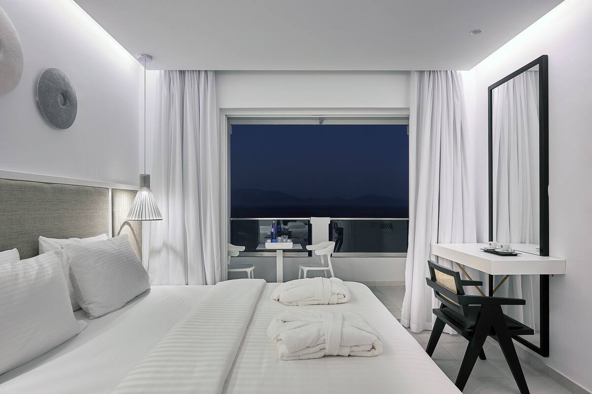 A modern hotel room with a large bed, a desk, and a view of the city at night.