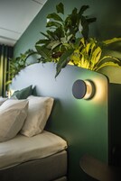 Una habitación moderna con una pared de acento verde, una cama con ropa de cama blanca y una planta en maceta en la pared.