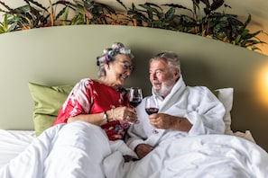 A couple in bed with a green headboard and a plant wall behind them.