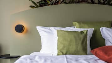 A neatly made bed with white and green pillows, a round wall-mounted light, and a small bedside table.