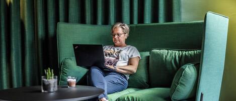 A person sitting on a green sofa with a laptop, a glass of water, and a glass of coffee on a small table in front of them.