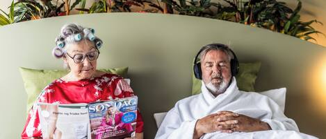 Two people sitting on a bed with a magazine, surrounded by plants.