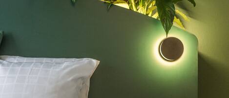 A bed with white bedding, a green wall, and a plant with green leaves.