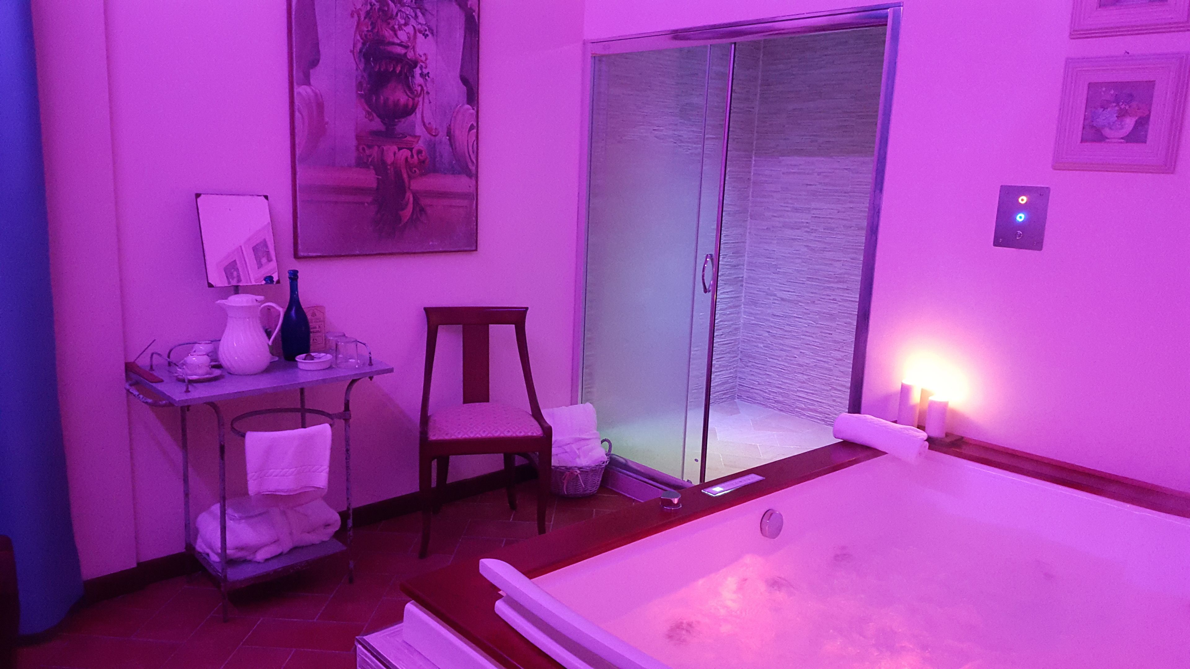 Une pièce dotée d’une grande baignoire, d’une chaise, d’une petite table avec un vase et une bouteille, et d’une porte-fenêtre coulissante donnant sur un balcon.